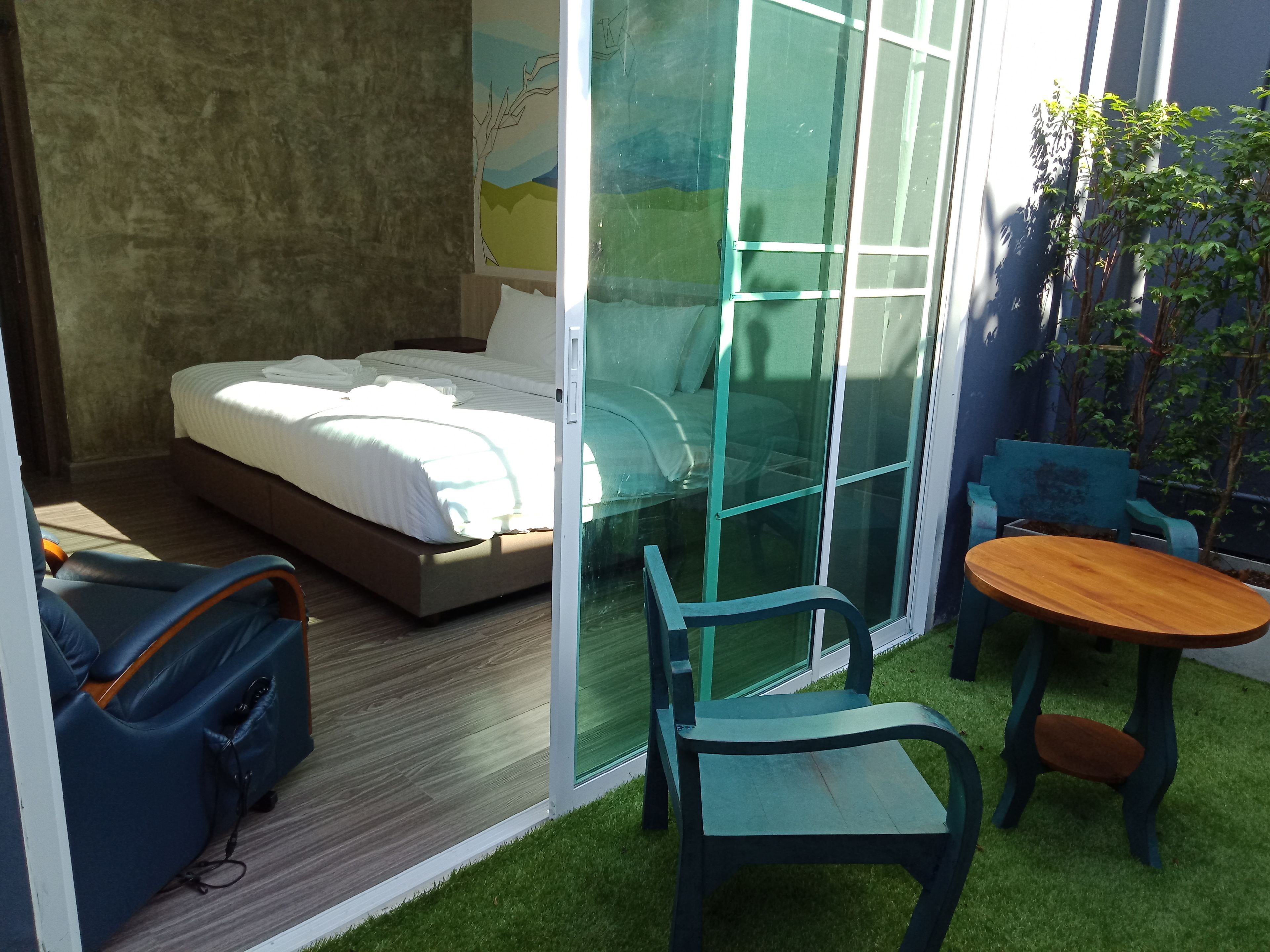 Un dormitorio con cama, una puerta corrediza de vidrio, una mesita, dos sillas y una maleta.