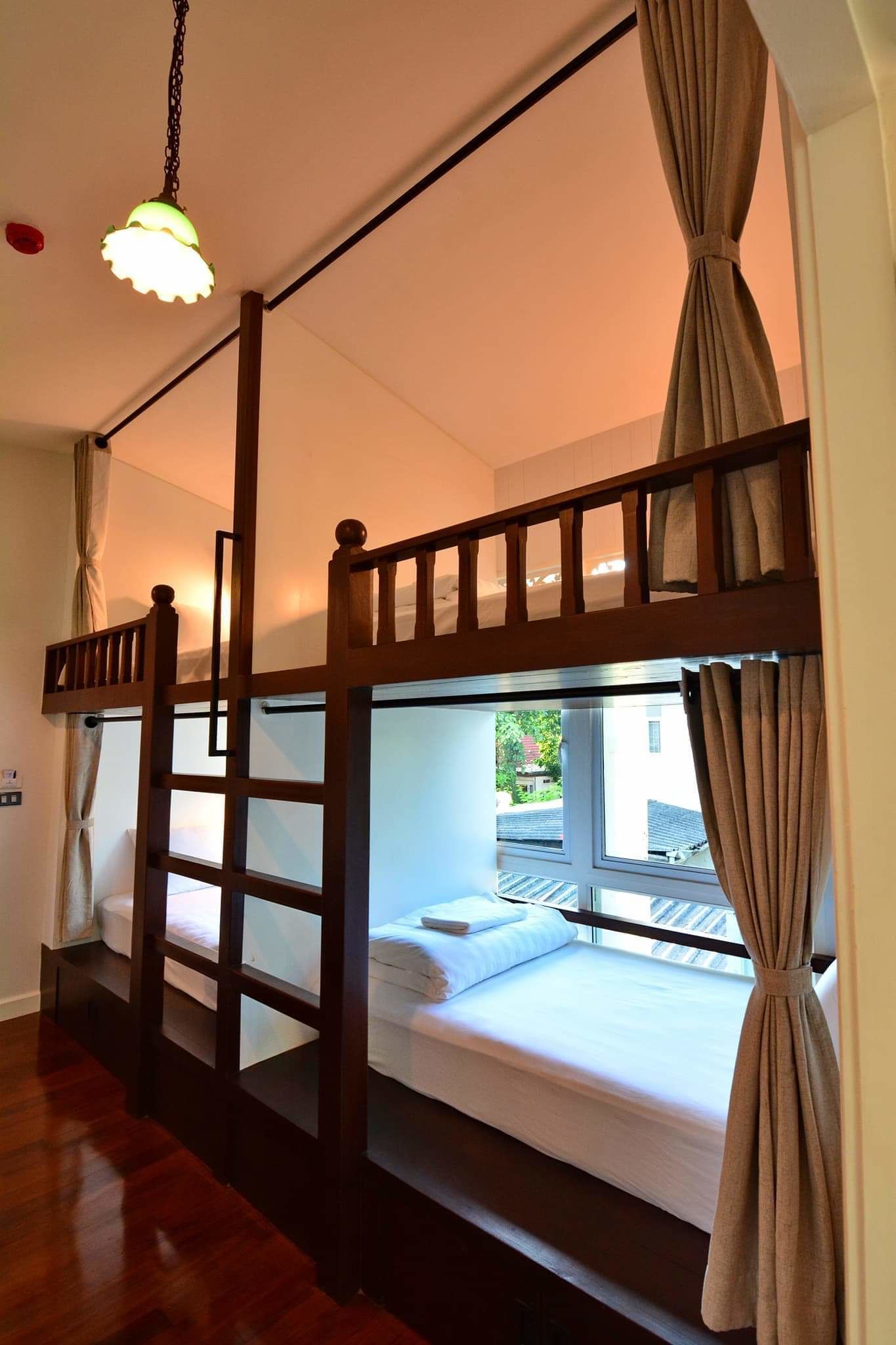 Una habitación con literas, barandillas de madera y una lámpara colgante.