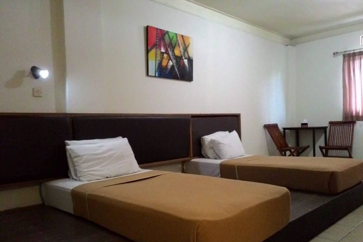 A hotel room with two beds, a small table, and a chair.