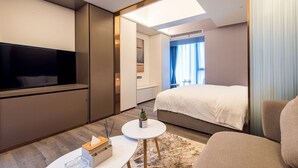 Una habitación de hotel moderna con una cama grande, un televisor de pantalla plana, una pequeña mesa redonda y una zona de estar.
