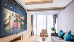 Una sala moderna con un televisor de pantalla plana grande, un sofá, una mesa de centro y una ventana con cortinas.
