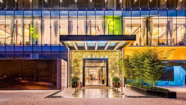 Una entrada de hotel moderna con puertas de cristal, un letrero en idioma extranjero y un interior bien iluminado.