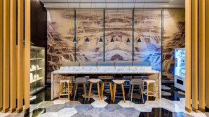 Un bar moderno con mostrador de mármol, taburetes de madera y un mural de un paisaje montañoso.