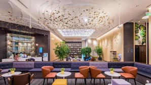Un vestíbulo moderno con una zona de estar central, una recepción y un techo decorado con elementos colgantes.