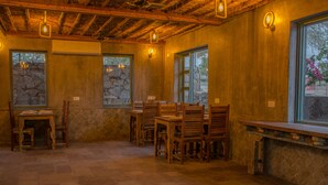 A rustic interior with stone walls, wooden tables and chairs, and large windows with stone frames.