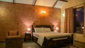 A bedroom with a wooden bed, a wicker chair, a brick wall, and a window with curtains.