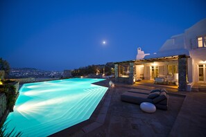Une villa moderne dotée d’une piscine, d’une architecture en pierre et offrant une vue sur la ville au crépuscule.