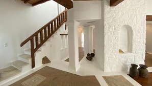 Um interior amplo com escada de madeira, paredes brancas e uma parede de pedra com um nicho.