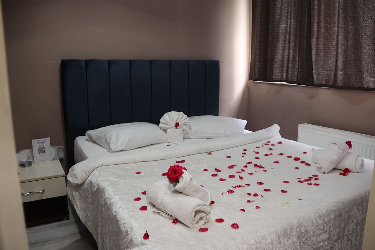 A neatly made bed with white linens, a blue headboard, and a bouquet of red flowers on the pillows.