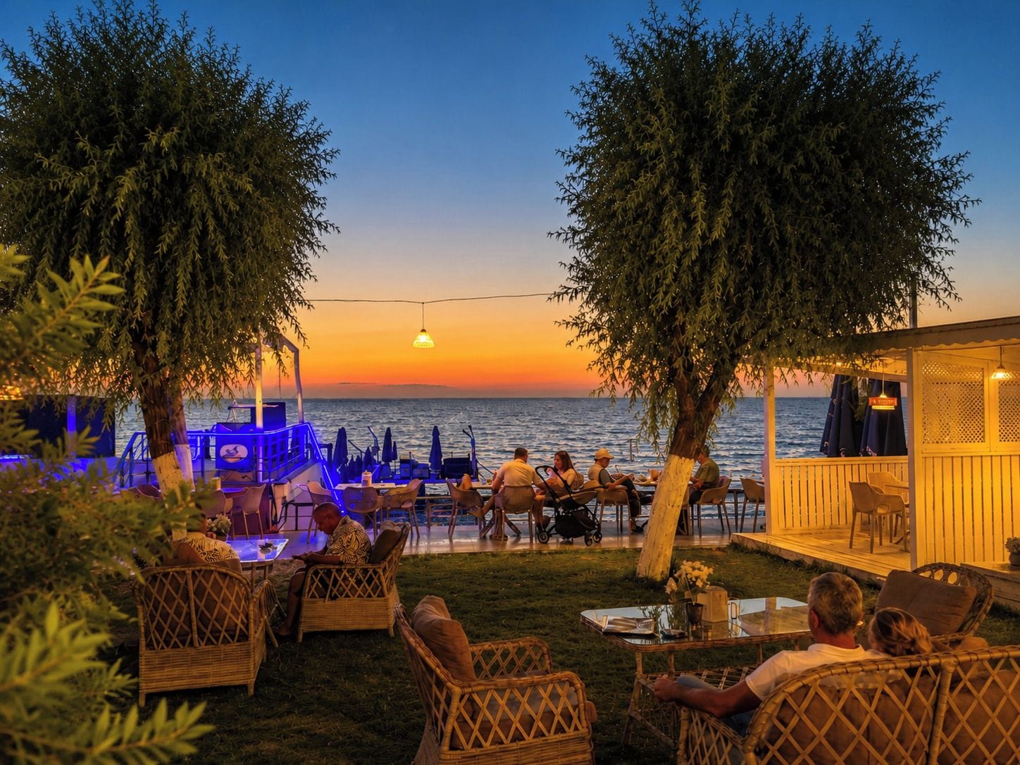 An outdoor seating area with tables and chairs, overlooking a body of water during sunset.