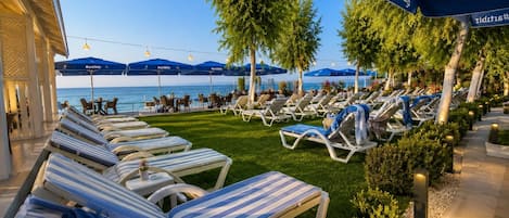 A seaside resort with sun loungers, umbrellas, and a view of the ocean.