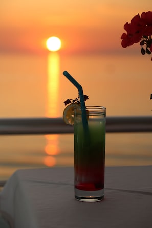 A glass with a straw and a slice of lemon on a table with a sunset view in the background.