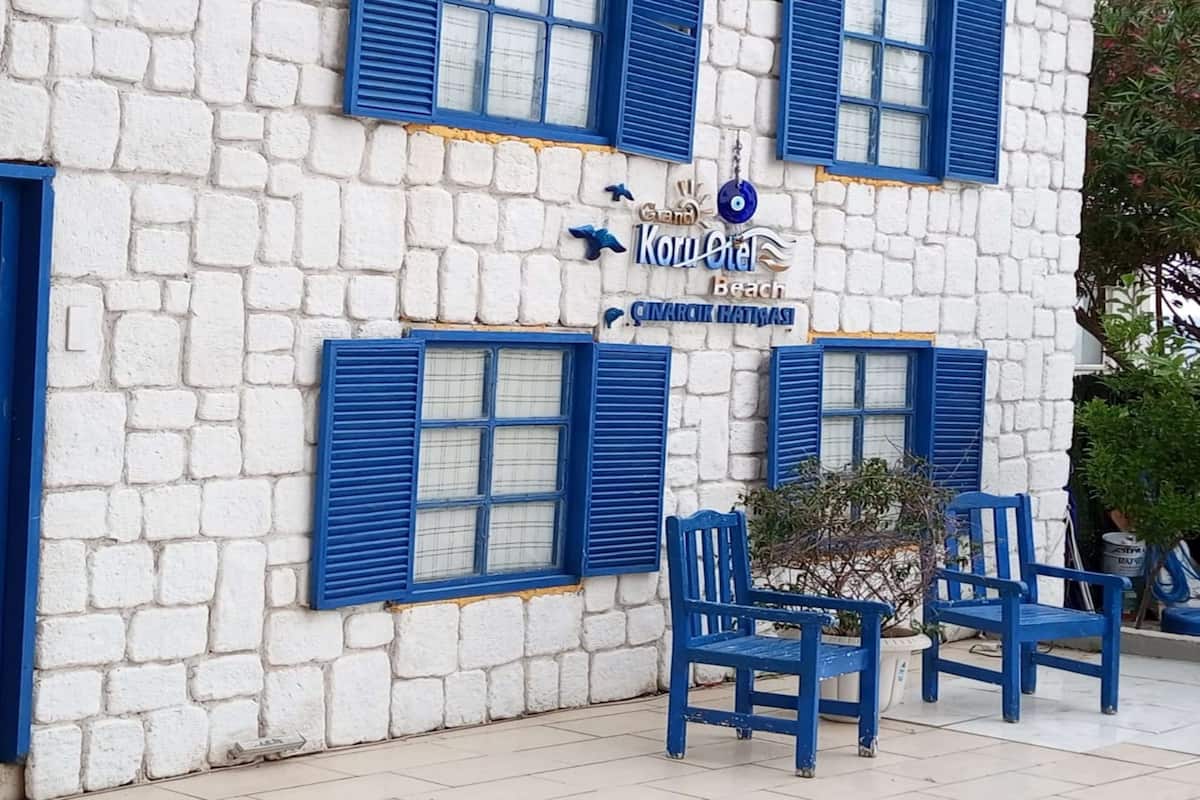 A building with white stone walls and blue shutters, featuring a sign that reads "Koru Hotel" and "Cinarcik Hatvas."