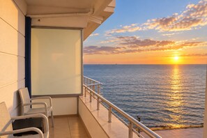 A balcony with a view of the sea at sunset, a white chair, and a metal railing. - Grand Koru Otel Beach (Cinarcik)