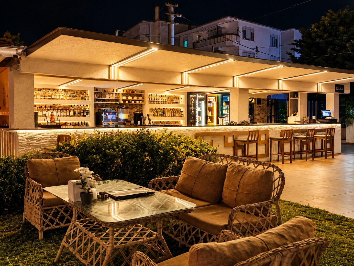 An outdoor bar area with wicker furniture, a glass table, and a bar stocked with bottles.