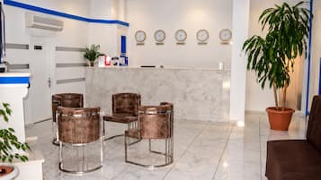 A hotel lobby with a reception desk, four leather chairs, a large potted plant, and clocks displaying times from various cities.