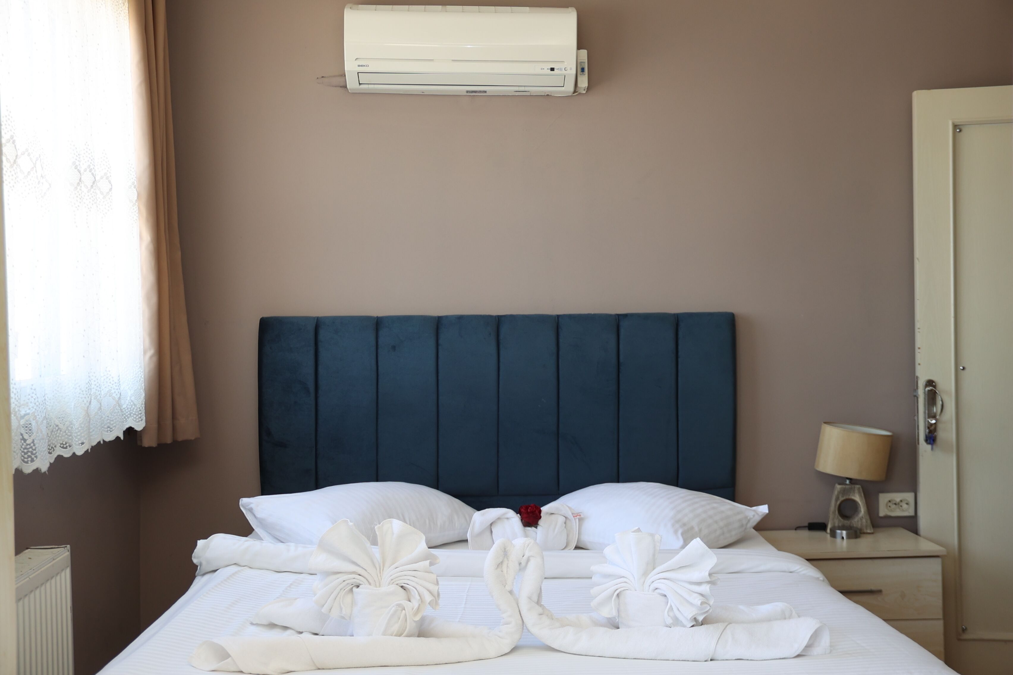 A hotel room with a bed, a nightstand, a lamp, and an air conditioning unit on the wall.