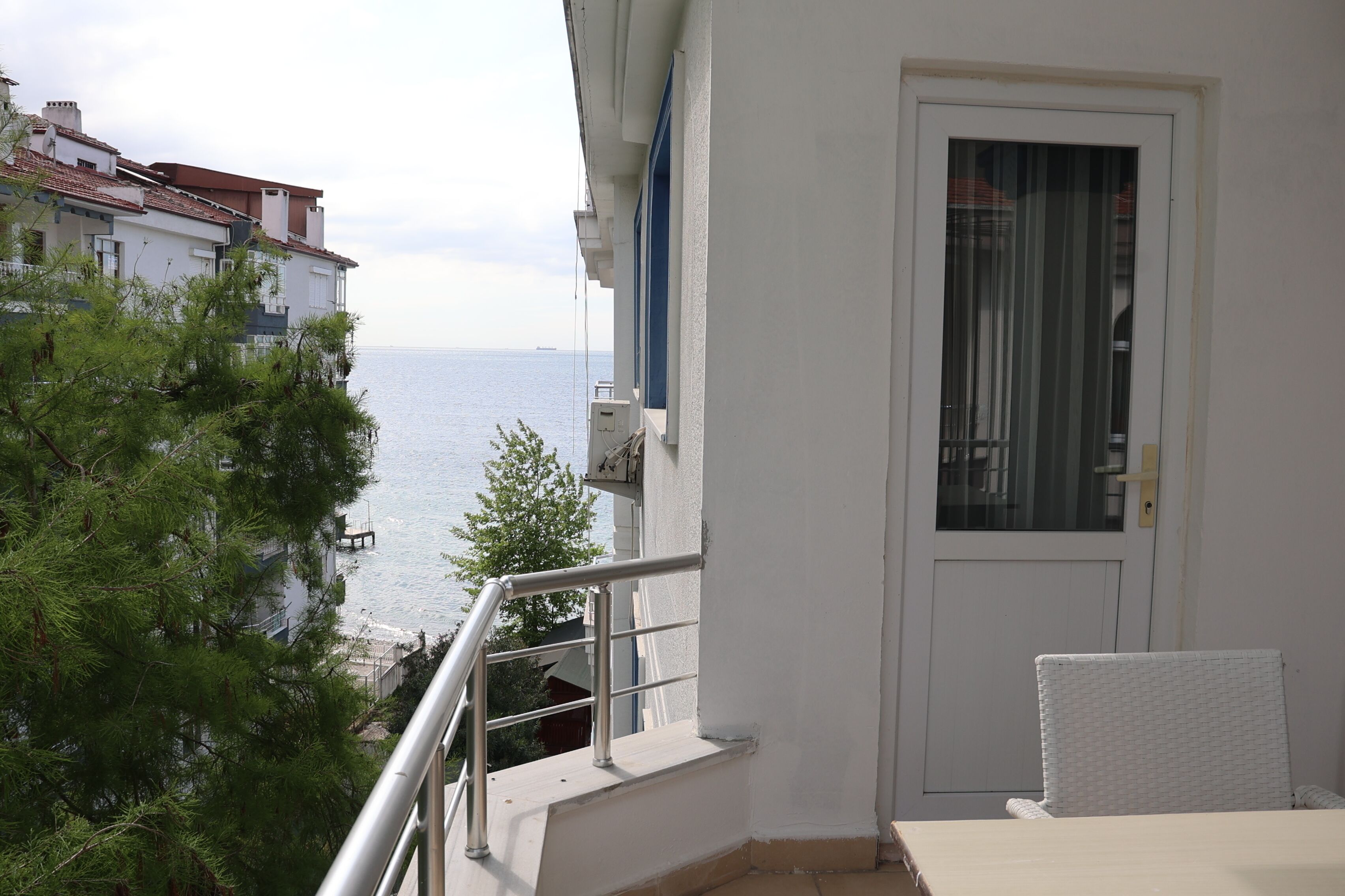 A balcony with a view of the sea, a white door, and a wicker chair.