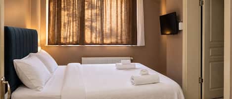 Een hotelkamer met een bed, een radiator, een raam met gordijnen, een flatscreen televisie en een deur.