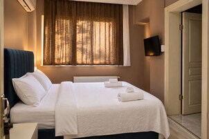 Habitación de hotel con cama, radiador, ventana con cortinas, televisor de pantalla plana y puerta.