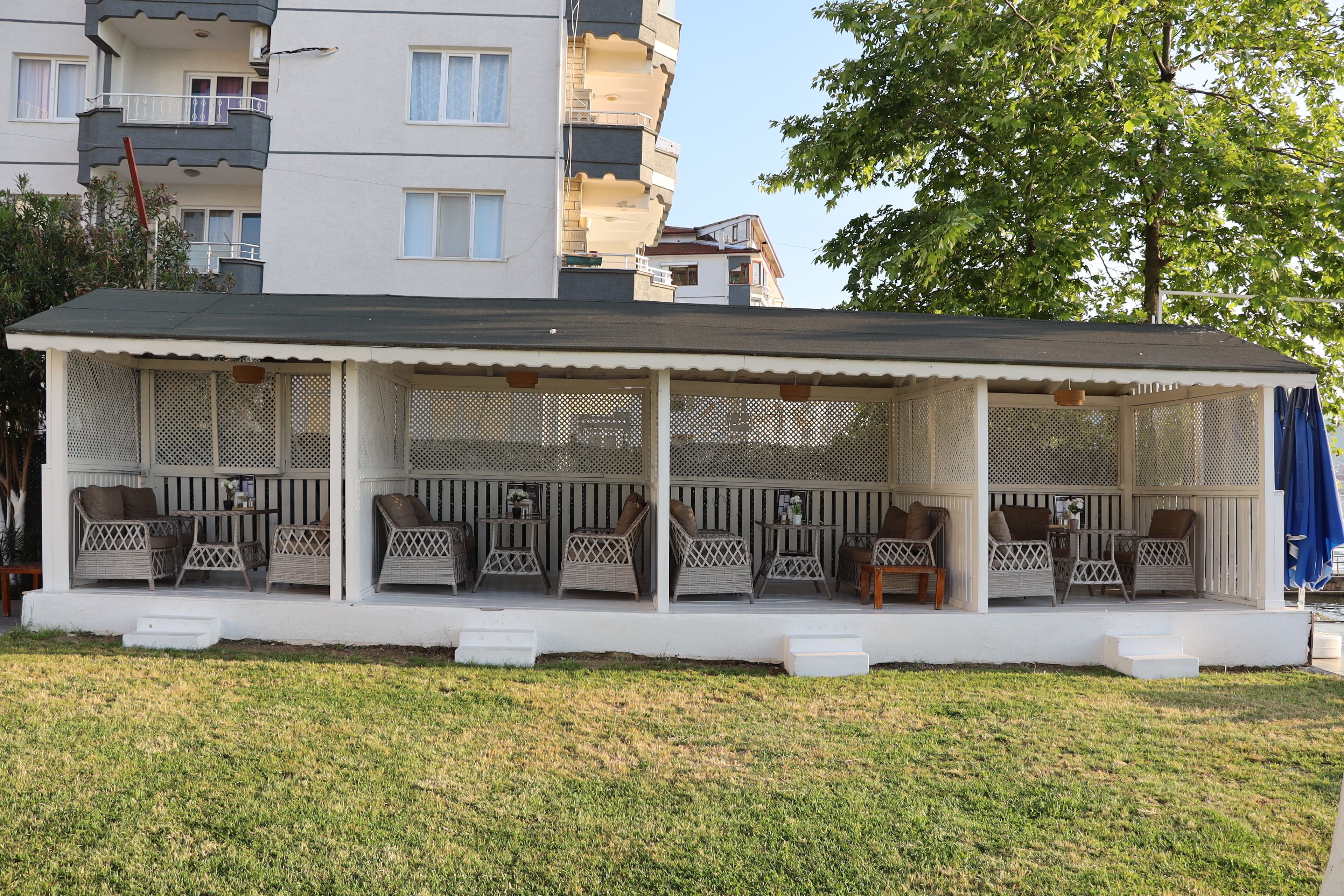 A covered outdoor seating area with wicker furniture and a white fence.