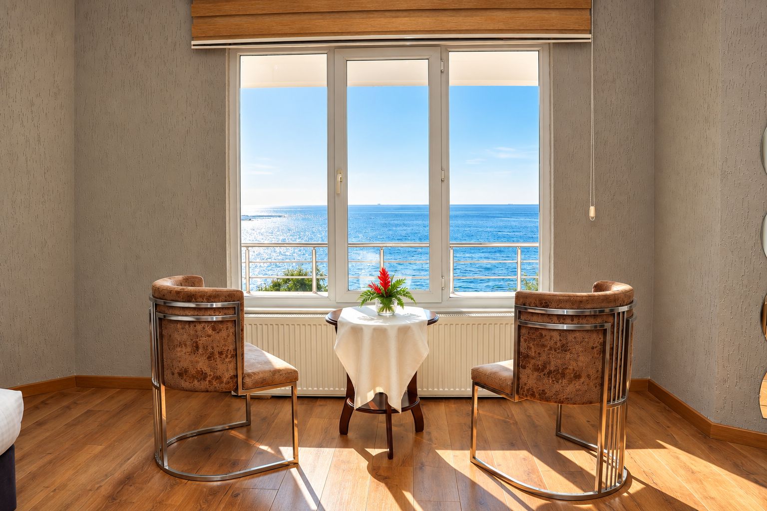 A room with two chairs, a table, and a view of the sea through a large window.