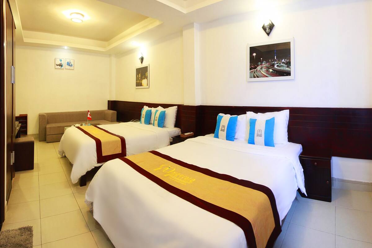 A hotel room with two beds, a sofa, a nightstand, and a wall-mounted picture.