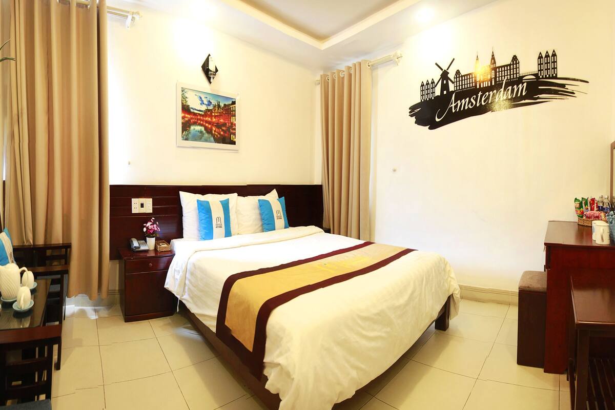 A hotel room with a bed, bedside table, lamp, and a wall with a cityscape mural.