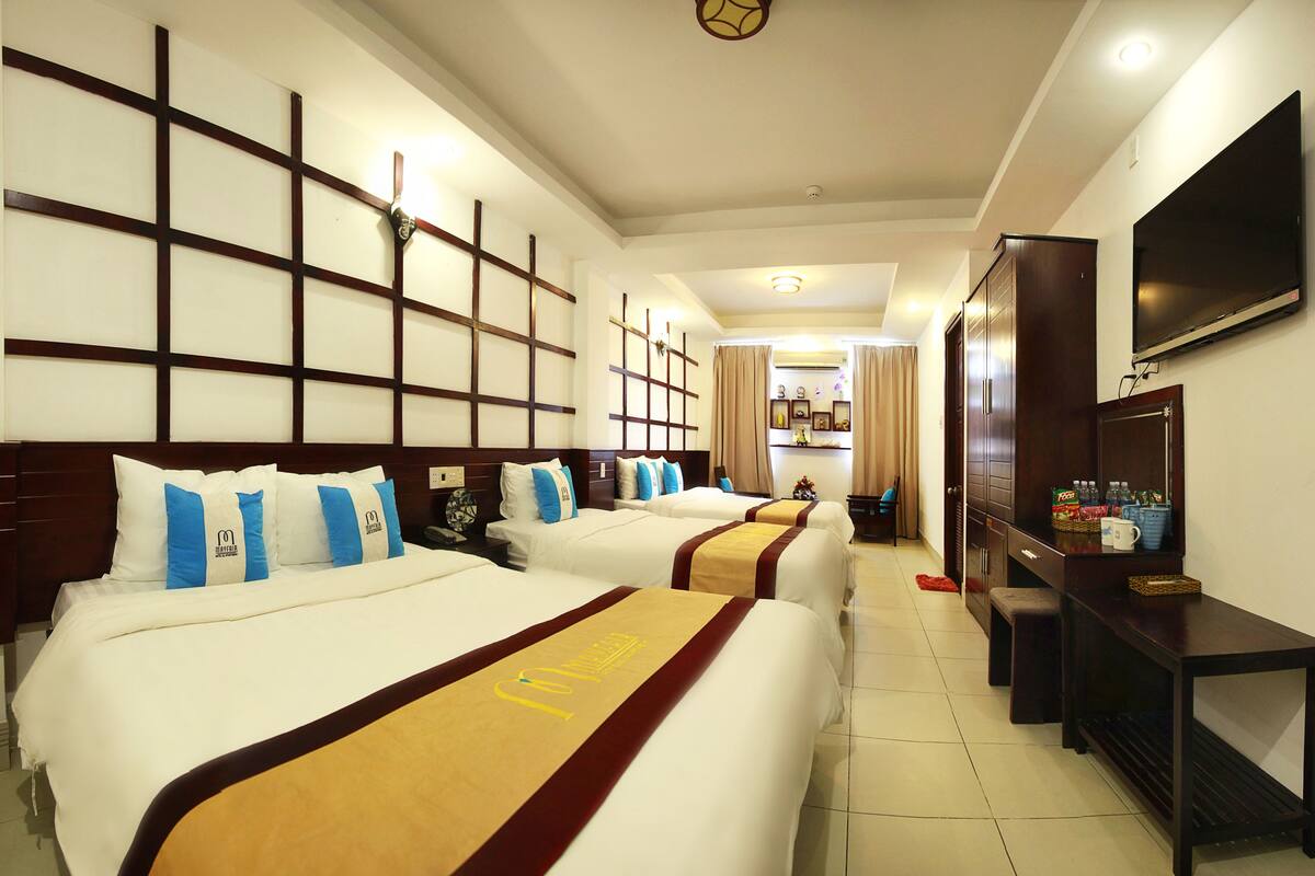 A hotel room with three beds, a TV, a desk, and a wardrobe.