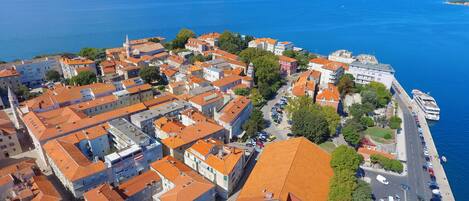 Vista aérea de un pueblo costero con edificios de tejas rojas, un puerto deportivo y una carretera que conduce al frente marítimo.