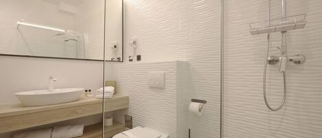 Un baño moderno con separador de vidrio, un lavamanos blanco, inodoro y ducha con cabezal de ducha manual.