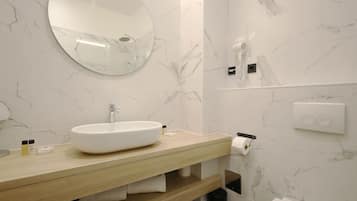 A modern bathroom with a marble wall, a round mirror, a sink, and a toilet.