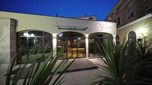 L’entrée d’un hôtel au design moderne, avec de grandes portes vitrées et une enseigne indiquant « TEATRO VERDI BOUTIQUE HOTEL ».