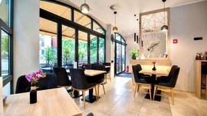 Un espace de restauration moderne doté de grandes fenêtres, de chaises noires, de tables en bois et de luminaires suspendus.