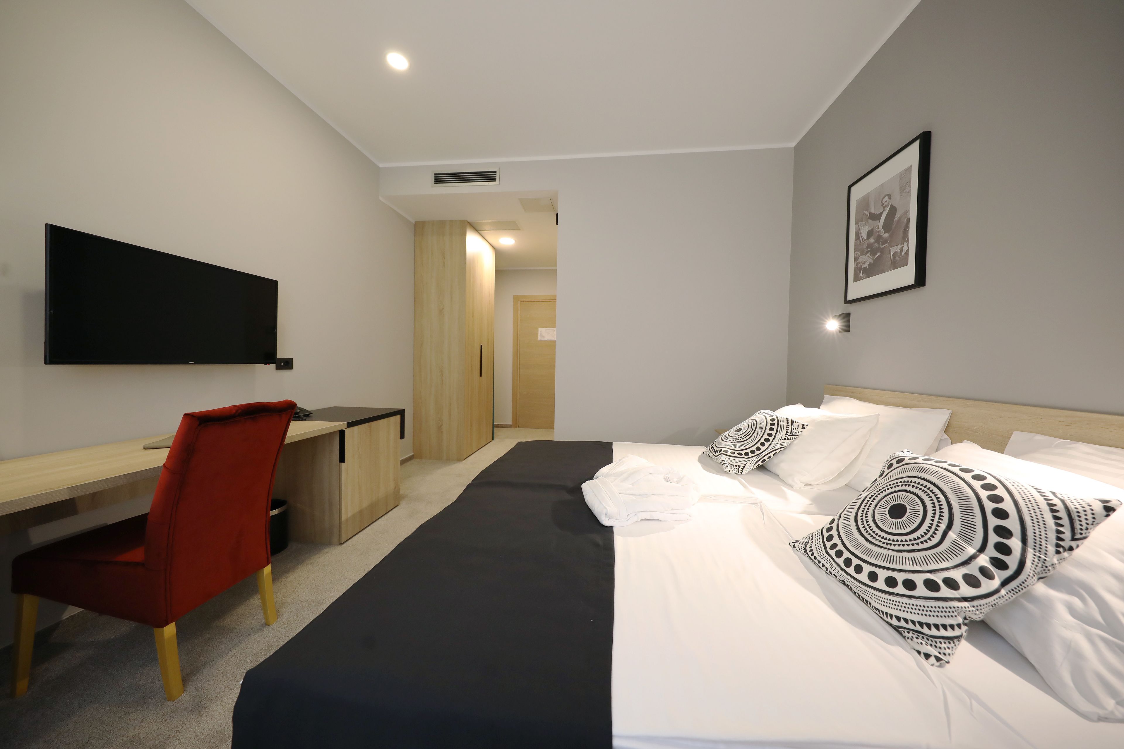 A hotel room with a bed, a desk, a chair, a TV, and a framed picture on the wall.