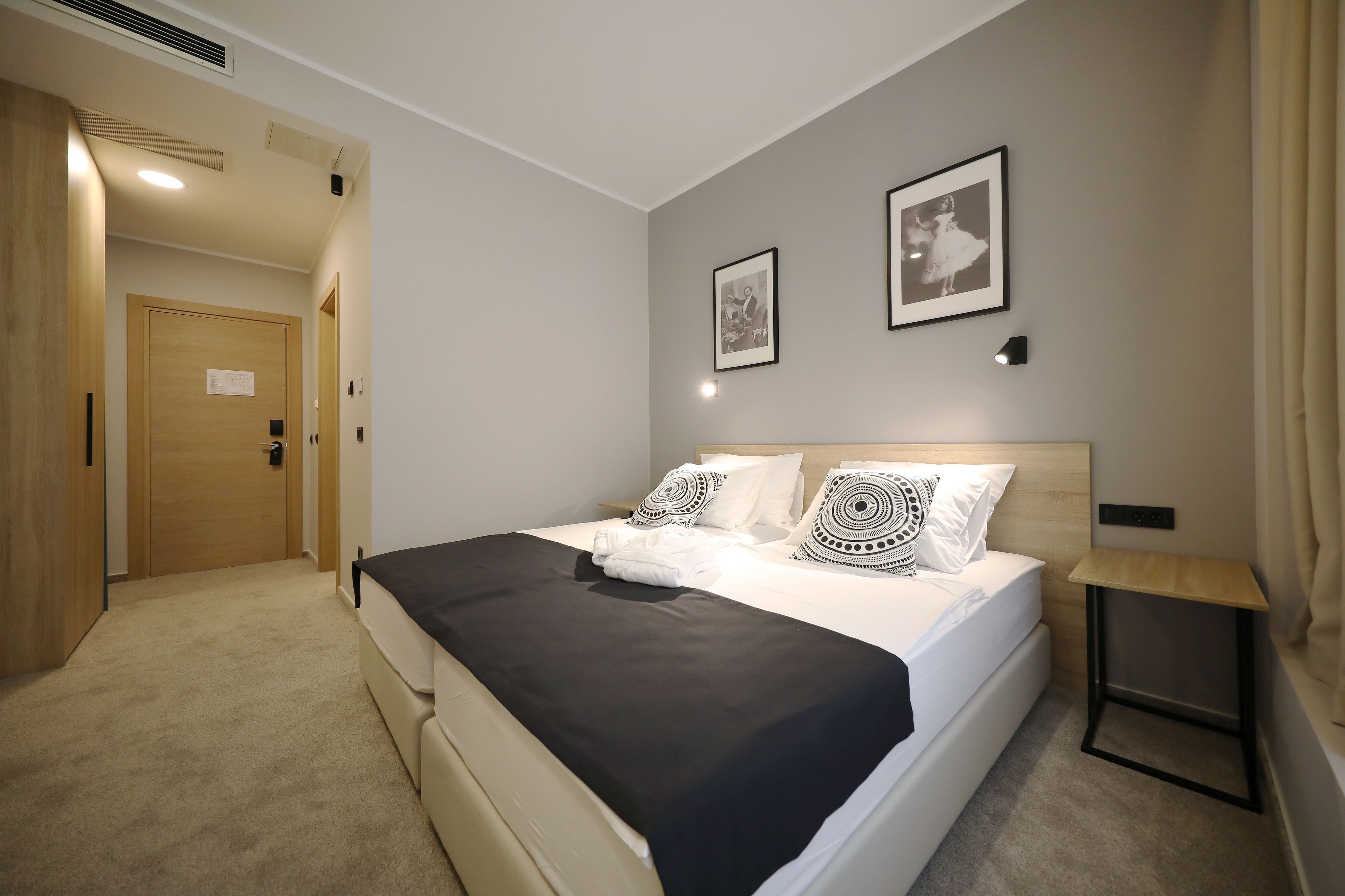 A hotel room with a bed, a bedside table, a door, and two framed pictures on the wall.