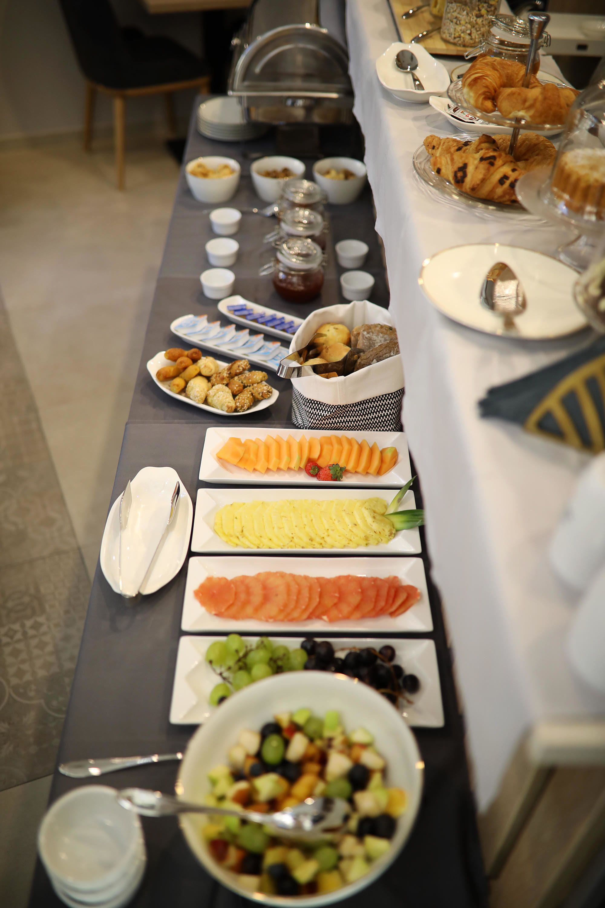 A buffet table with various food items including fruits, pastries, and condiments.