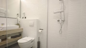 Un baño moderno con cabina de ducha de vidrio, inodoro blanco y tocador con espejo.