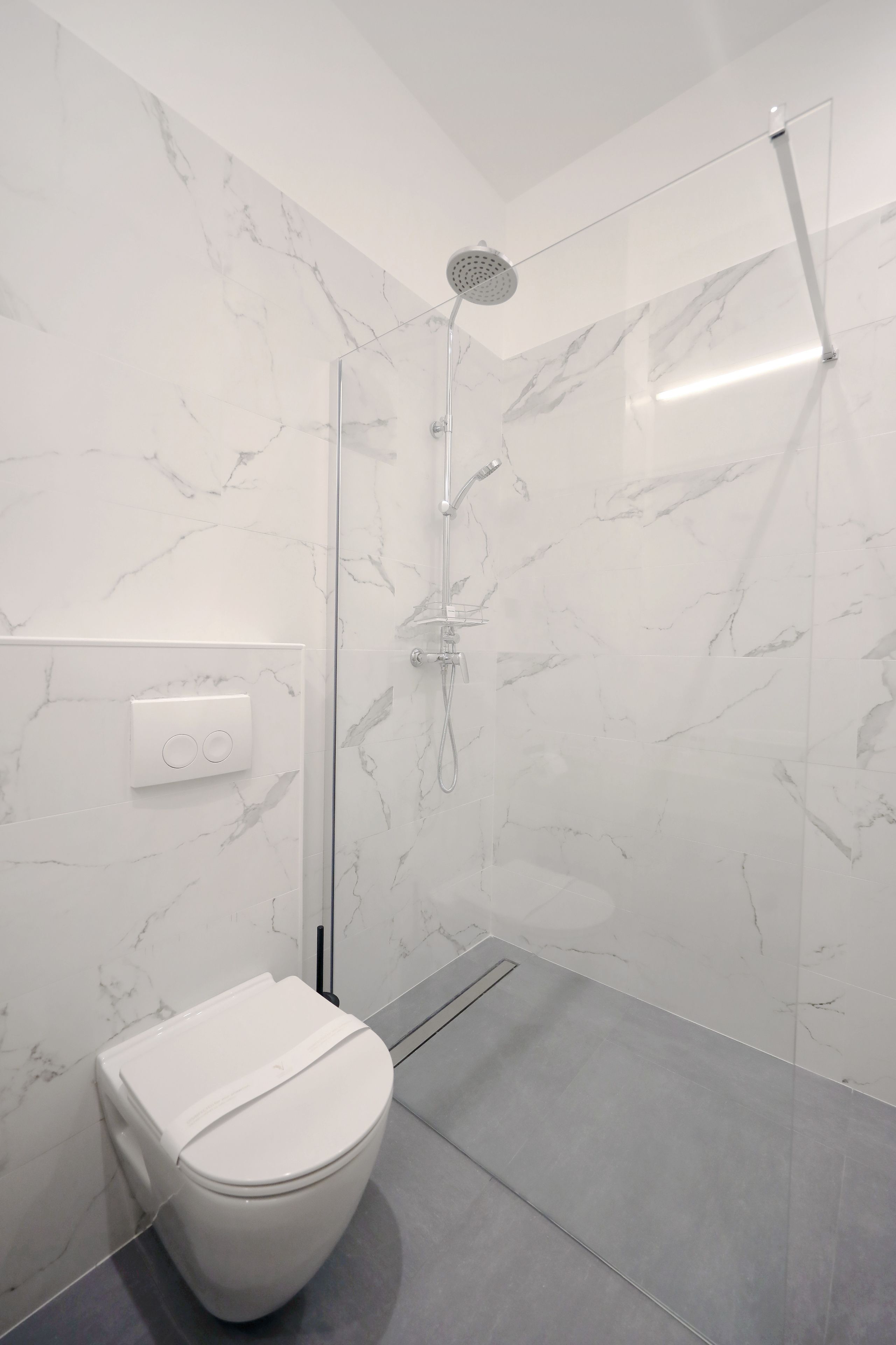A modern bathroom with a glass-enclosed shower, a white toilet, and marble-patterned walls.