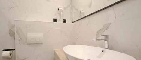 Un baño moderno con pared de mármol, lavabo blanco y retrete.