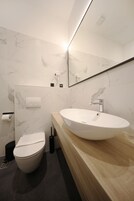 A modern bathroom with a marble wall, a white sink, and a toilet.