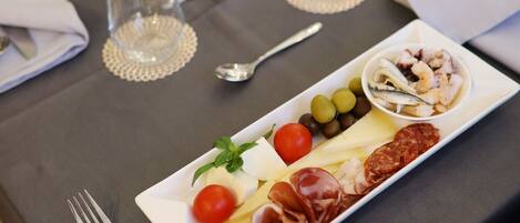 A dining table with a variety of food items, including meats, cheeses, and olives, along with cutlery and glasses.