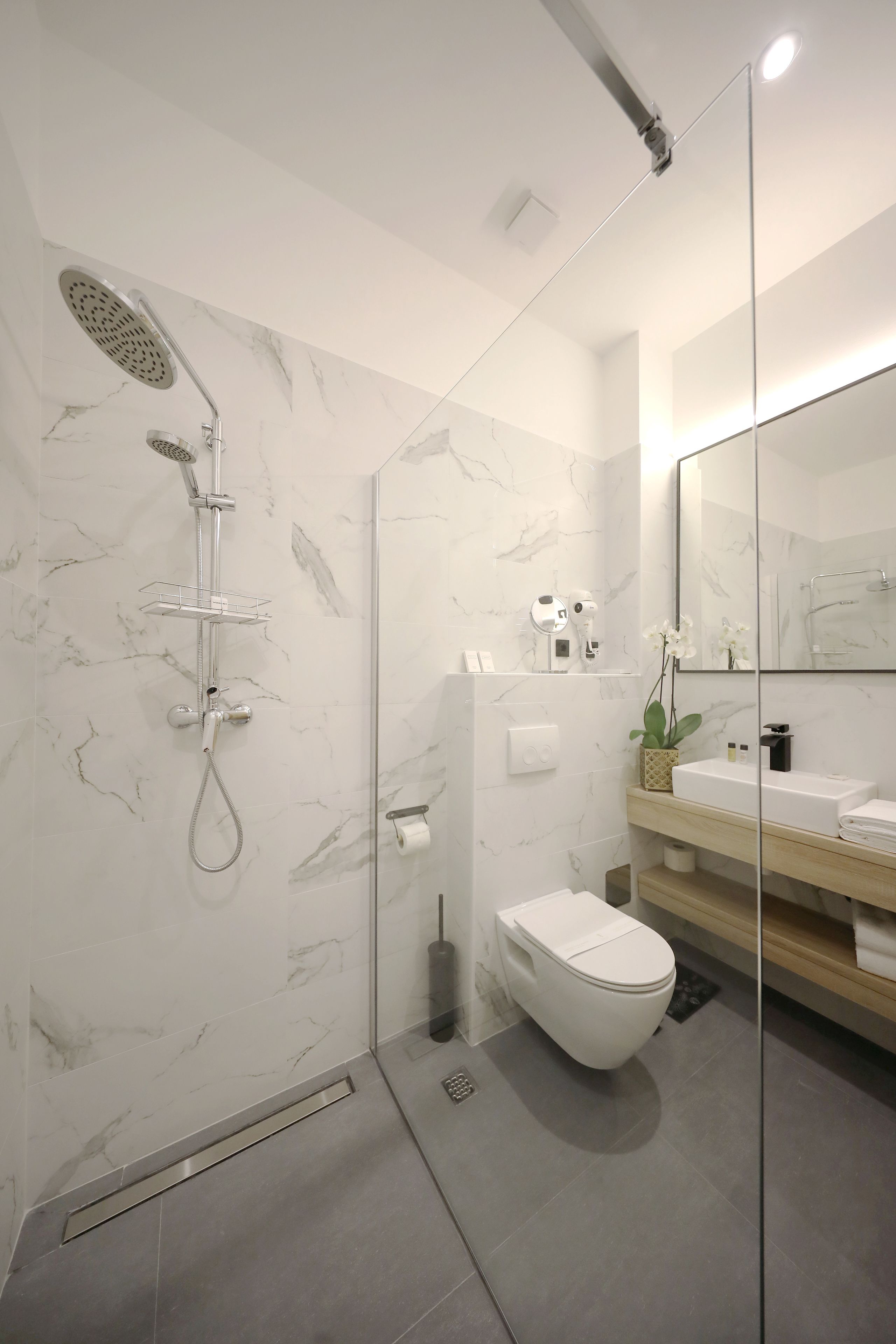 A modern bathroom with a glass shower enclosure, a white toilet, a sink with a mirror, and marble-patterned walls.