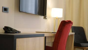 Habitación de hotel con televisión de pantalla plana montada en la pared, un escritorio con lámpara, una silla roja y una silla negra.
