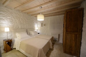 A bedroom with two beds, a wooden wardrobe, a radiator, and a lamp on a wooden nightstand. - Villa Ammonite (Mykonos)