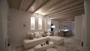 A modern living room with a sectional sofa, a coffee table, and a dining area in the background. - Villa Ammonite (Mykonos)