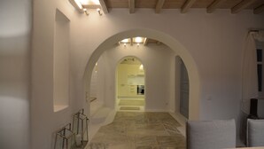 A hallway with an arched ceiling, a stone floor, and a view into a kitchen area. - Villa Ammonite (Mykonos)