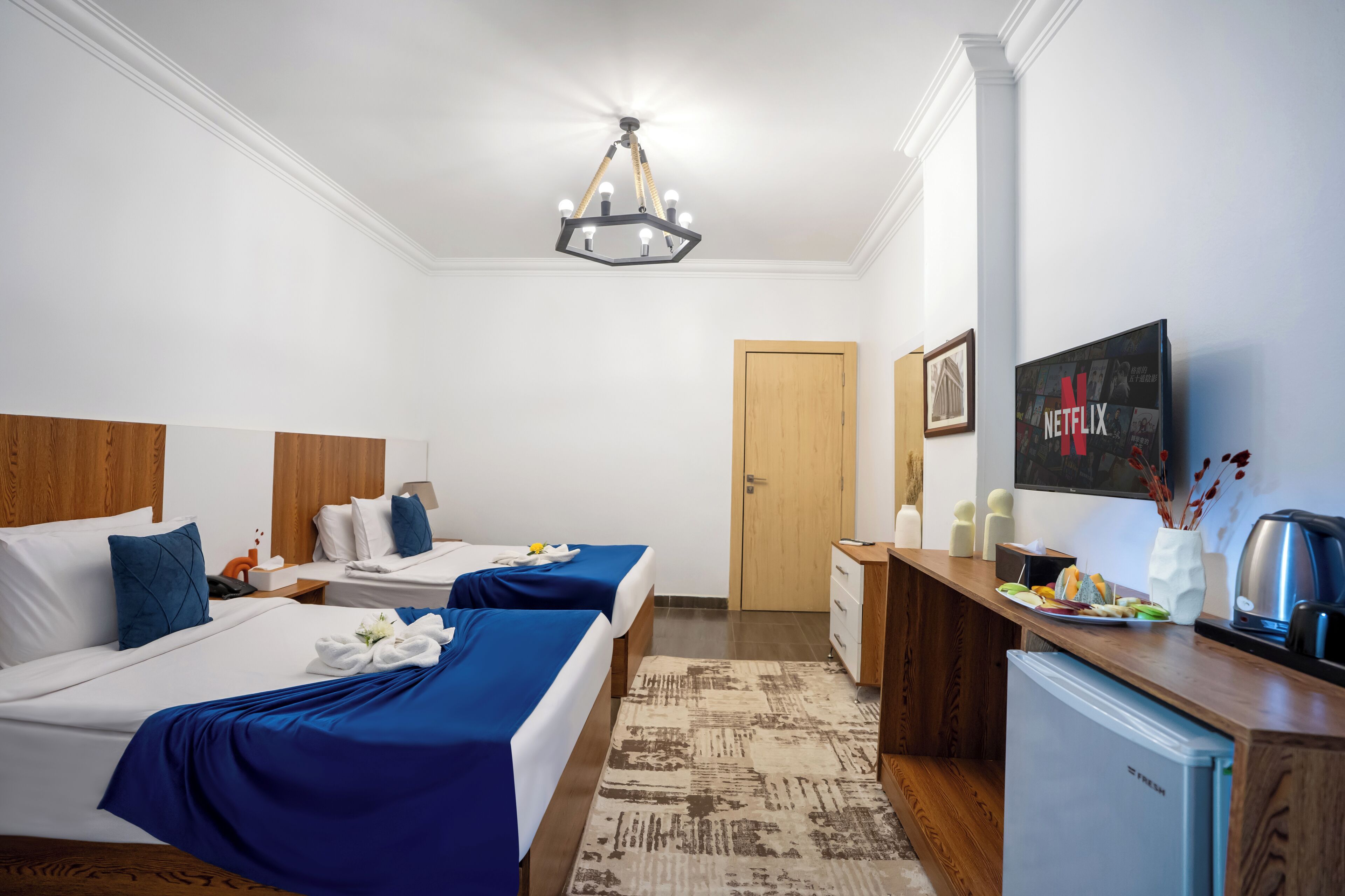 A hotel room with two beds, a minibar, a television, and a door.