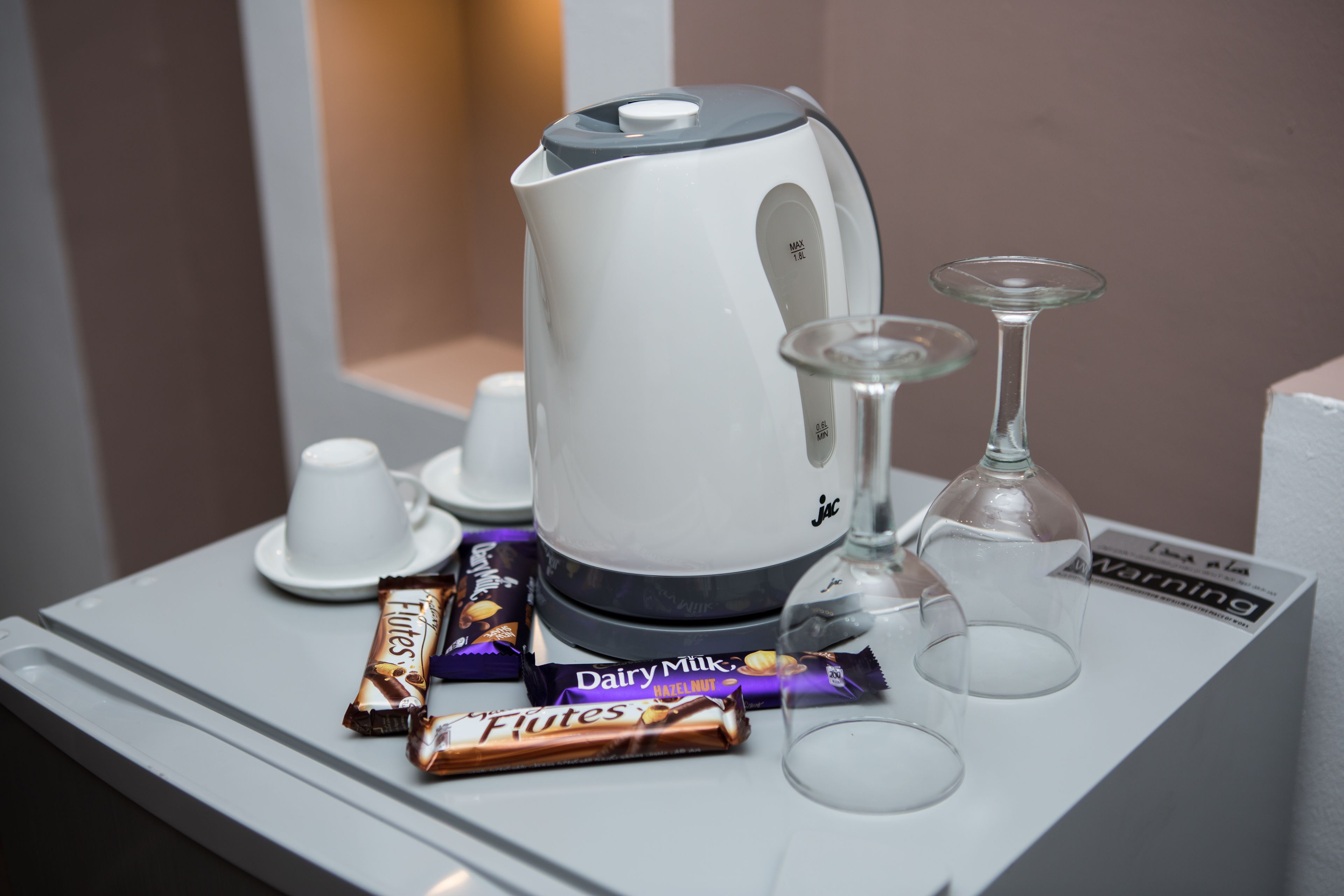 Une bouilloire blanche, deux verres et deux tablettes de chocolat sur un plateau.
