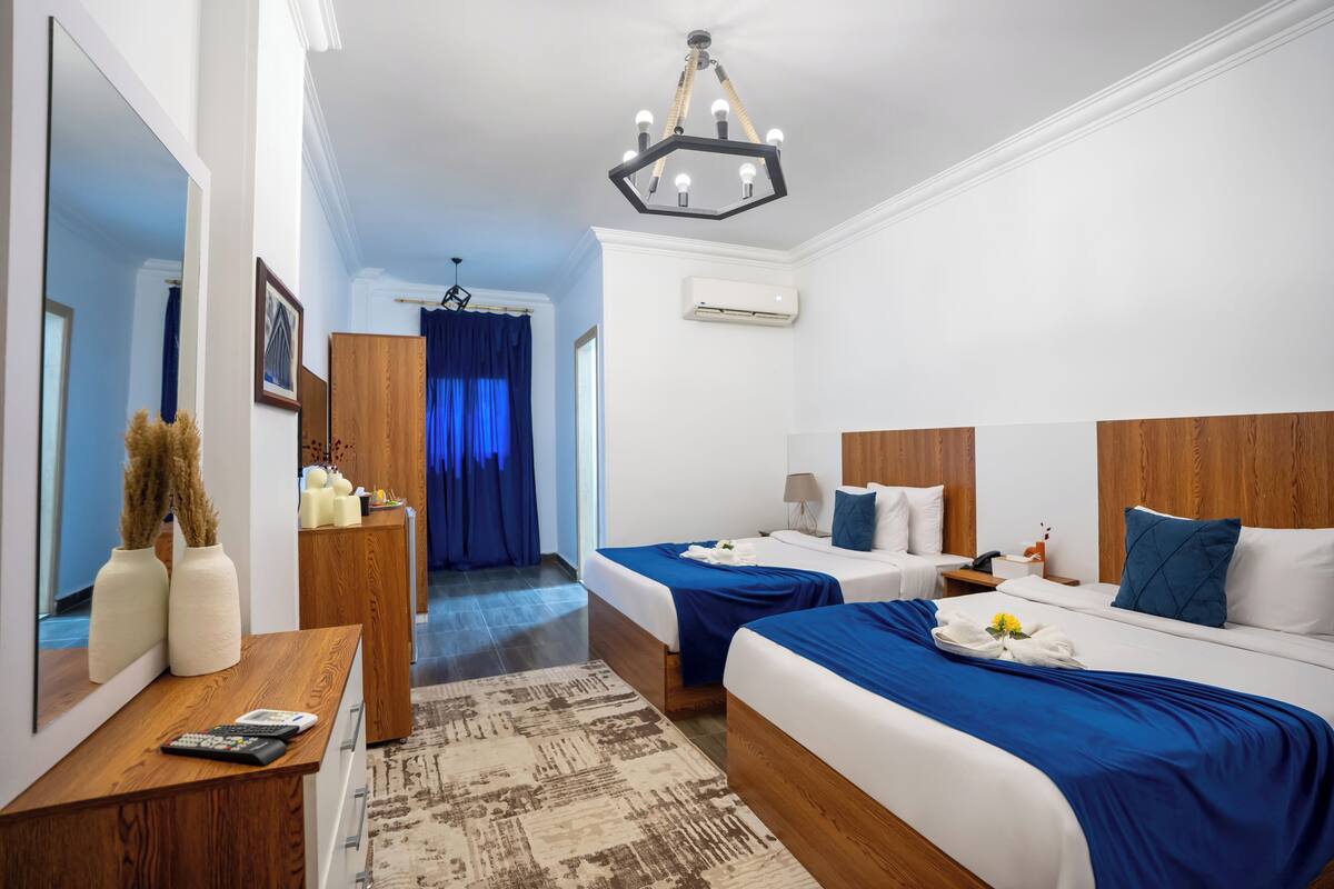 A hotel room with two beds, a wooden desk, a mirror, and a chandelier.